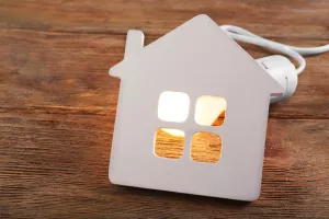 Bulb and shape of home on wooden background<br>električna energija, kuća, kuće, kućanstva, kućanstvo, opskrba struja