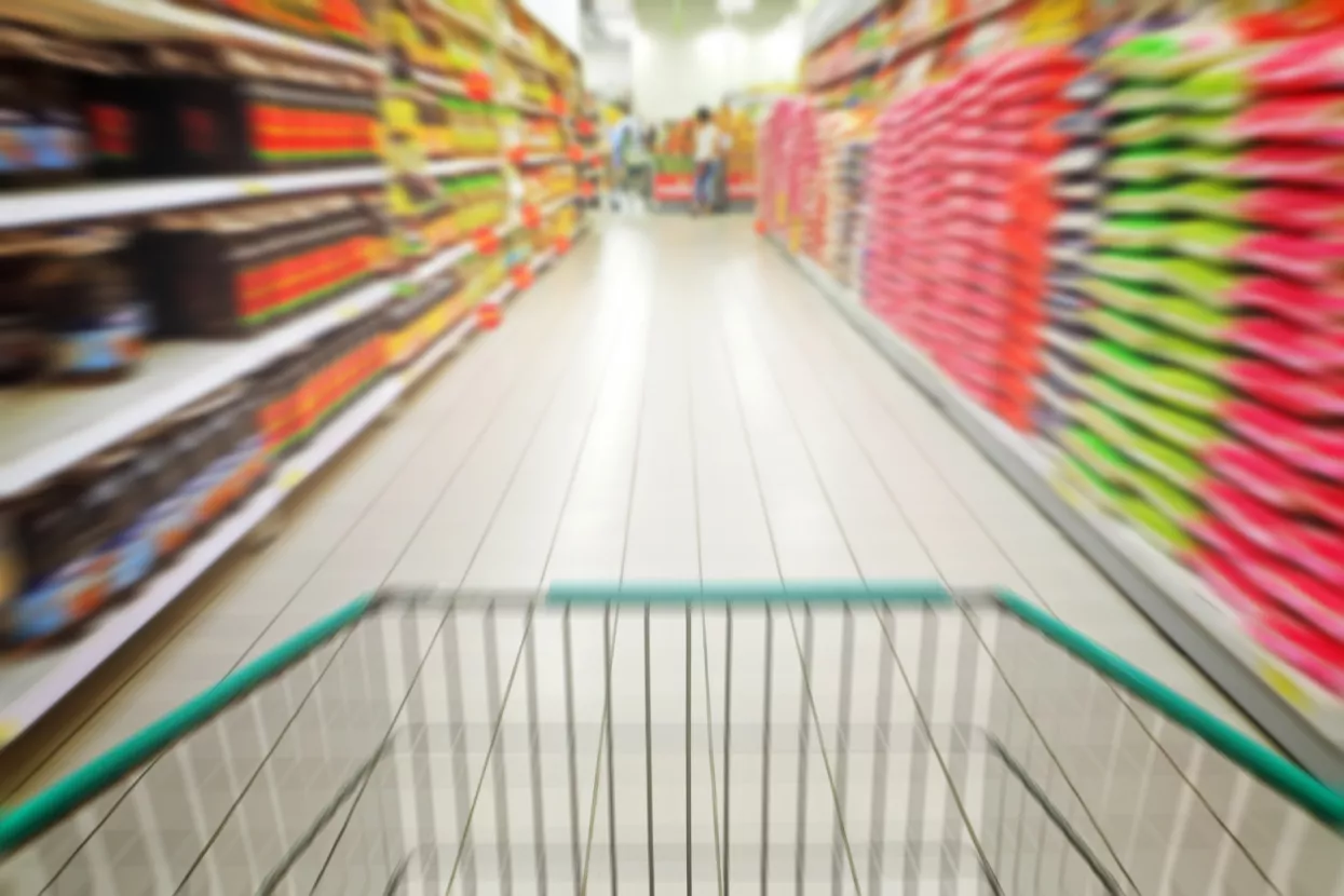 A zoom perspective view of a shopping cart wheeling through a supermarket aisle.