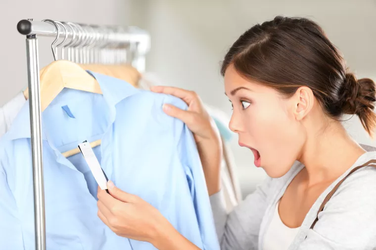 Shopping woman shocked over price tag. Funny shopper woman staring amazed at price. Mixed race Caucasian/Asian Chinese young female model in clothing shop.