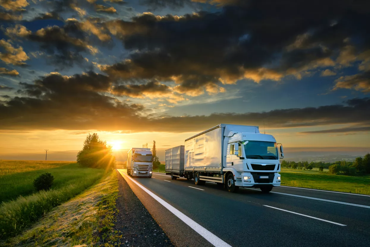PRILOG<br>Transport, &scaron;pedicija i izvoznici<br>Overtaking trucks on an asphalt road in a rural landscape at sunset