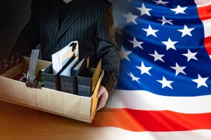 Unemployed. Man holds a box with personal belongings. USA flag. Concept - unemployed American. American was fired. USA resident is unemployed. Stationery in a cardboard box. American labor market amerika<br>sad, zaposlenost, stopa zaposlenosti, posao, poslovi