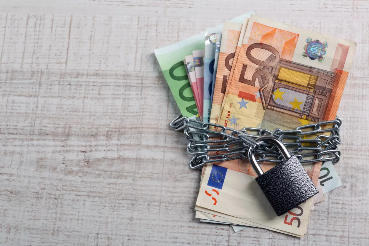 Euro banknotes with lock and chain on wooden table background