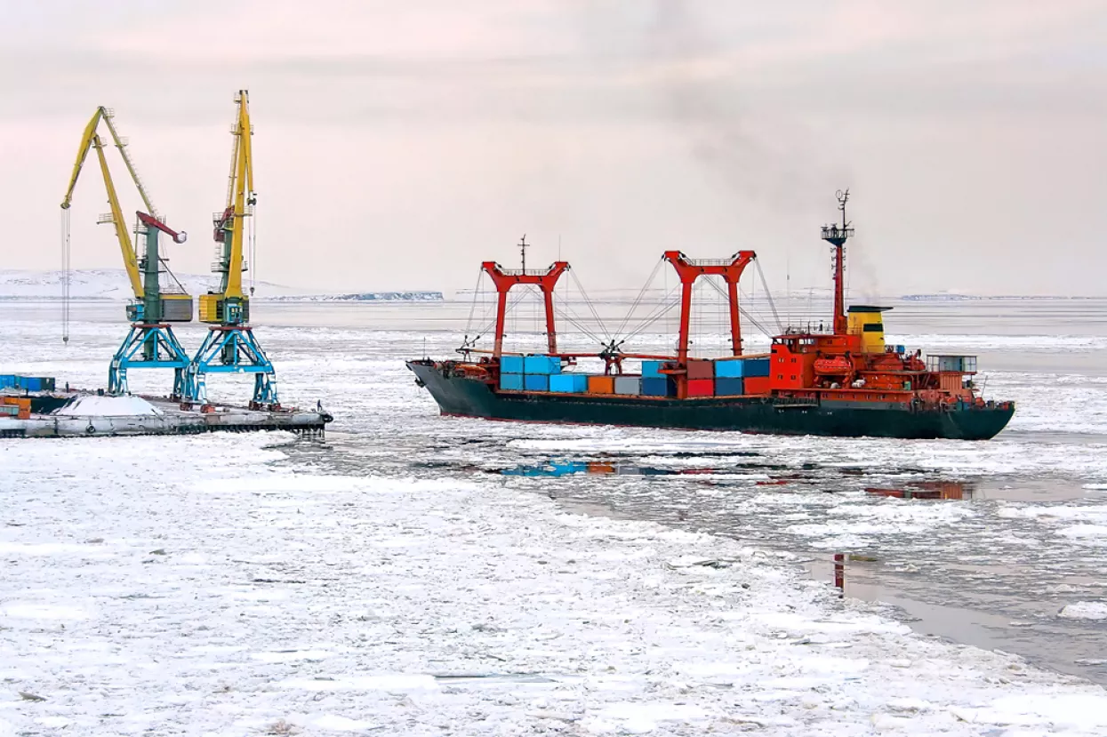 A cargo ship with containers near the pier of the seaport. Maritime navigation and shipping in the Arctic. The ship passes among the ice floes. Anadyr Sea Port, Chukotka, Far East Russia. November.