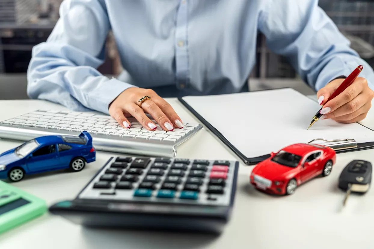 Businesswoman working on documents with small cars calculators and keys on the table. The concept of car insurance