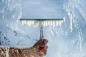 Window cleaner using a squeegee to wash a window with clear blue sky backgroundči&scaron;ćenje, outsourcing, vanjske usluge, pomoć
