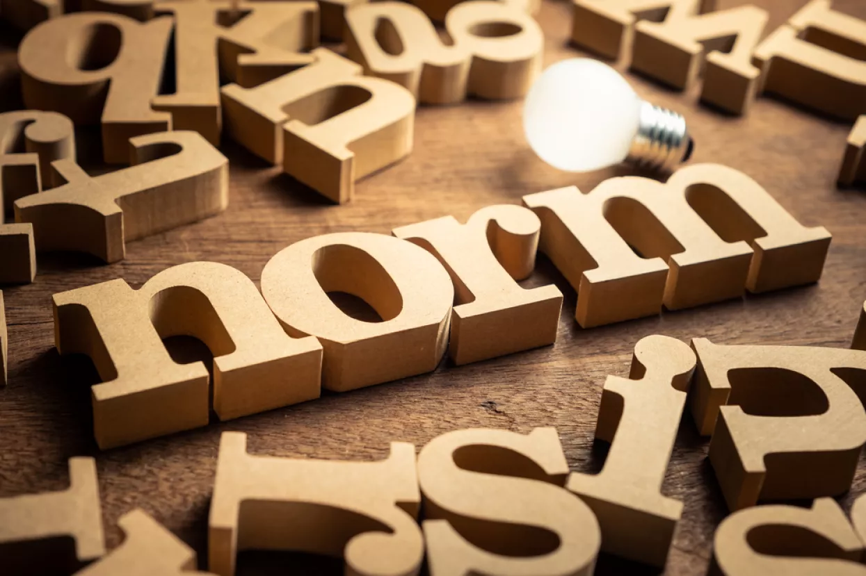 NORM word by wood alphabets with many random letters around and glowing light bulbnorma, norme, pravila, pravilo