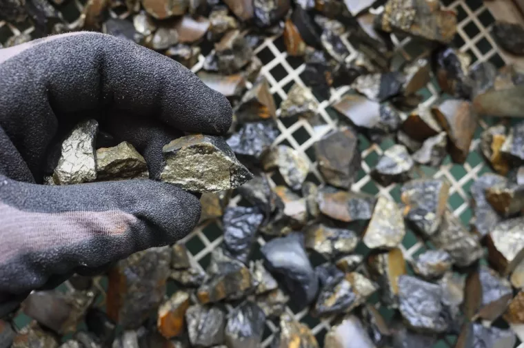 Mine, mining of tin (Sn) ore, as mineral cassiterite (SnO2). Rocks held in gloved hand. Element used in Lithium-ion batteries, coils of superconducting magnets, pigments, solder, plating and bronzekositar, metal