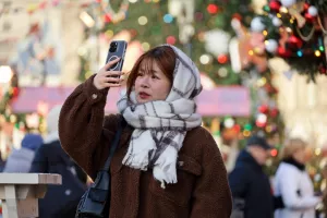 Moscow, Russia - December 5, 2024Asian girl taking pictures on smartphone camera standing on New Year trees background, tourist in winter cityAzija, azijatkinja, turisti, turistkinja, turizam
