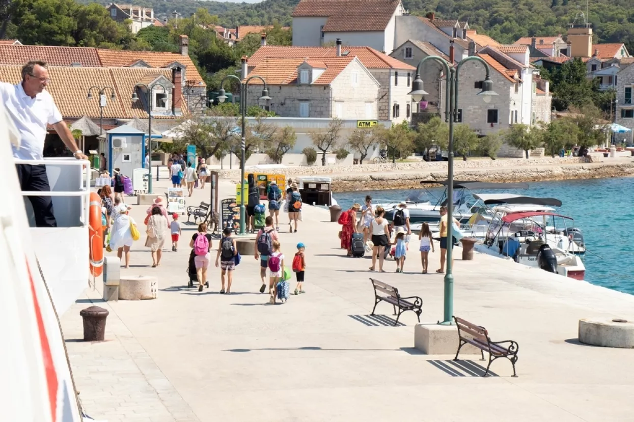Zlarin island, Croatia - July 22, 2022People leaving the pier, and a man working on a Jadrolinija ferry watching from the deckturizam, turistička sezona