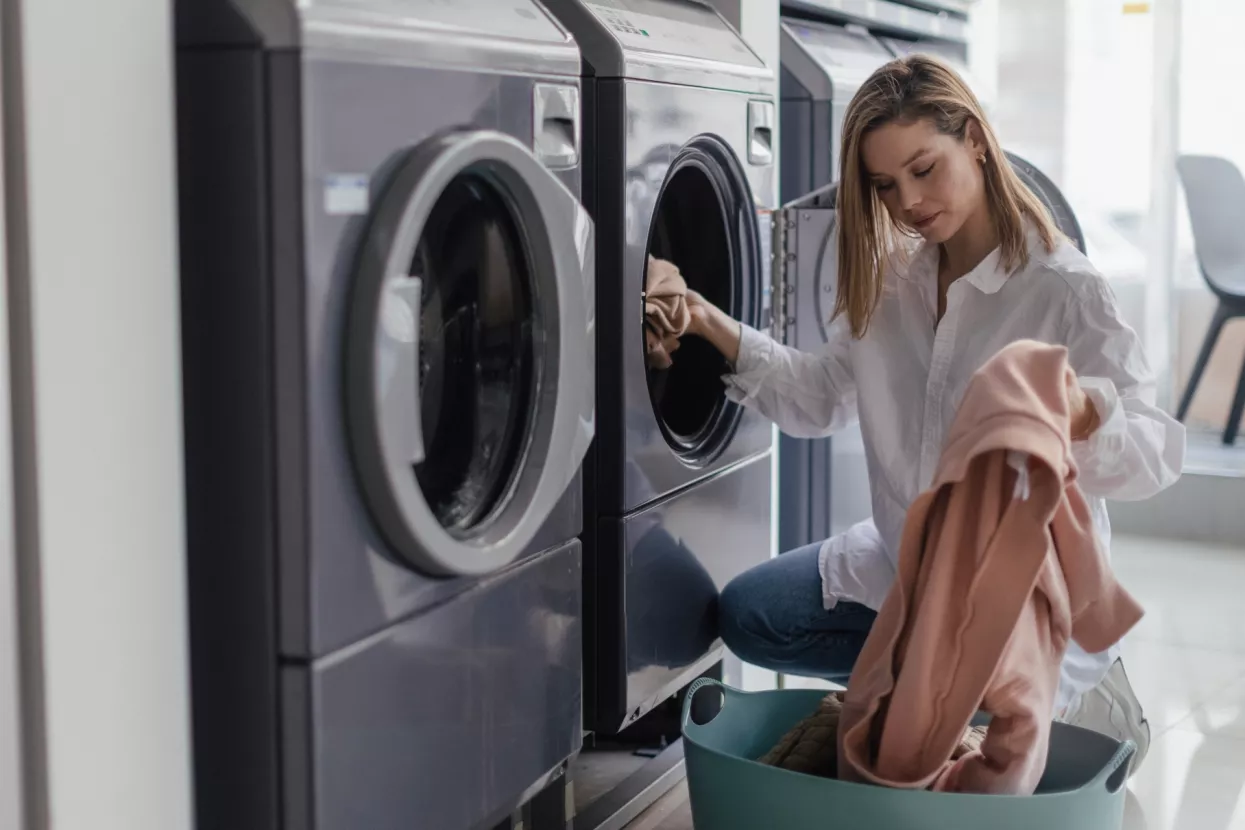 Young woman loading washing machine in public laundry.