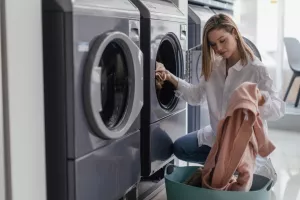 Young woman loading washing machine in public laundry.